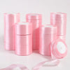 Rolls of pink silk satin ribbons stacked and unrolled on a white surface.