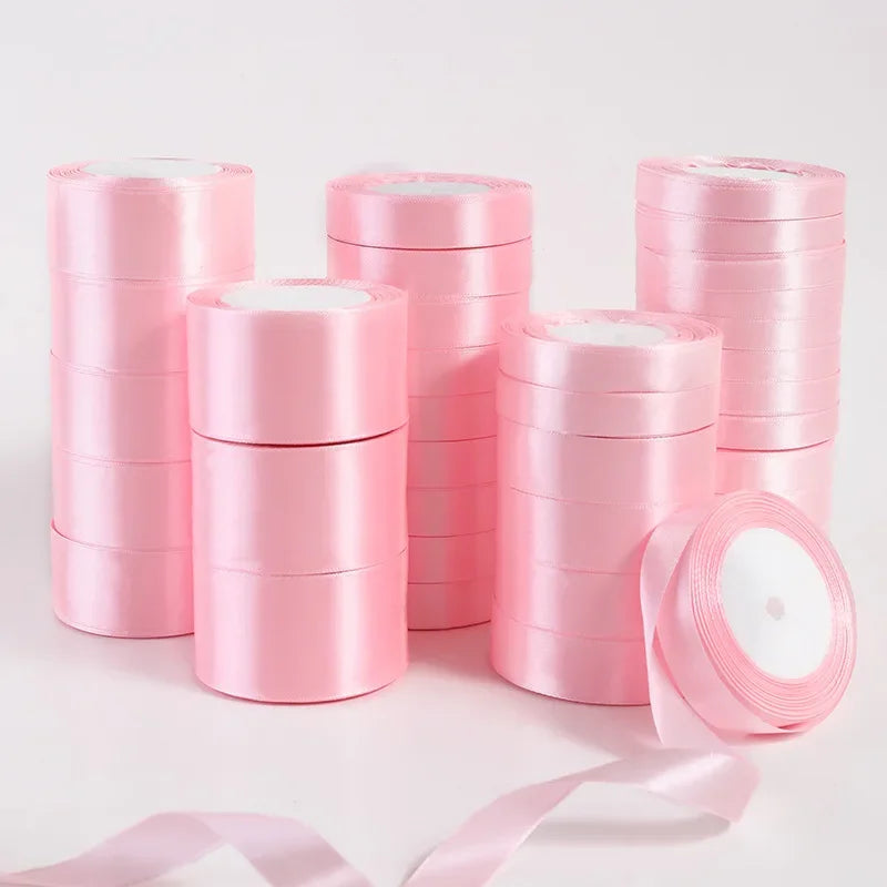 Rolls of pink silk satin ribbons stacked and unrolled on a white surface.