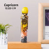 A tall glass bottle filled with natural crystals and a yellow top, representing Capricorn zodiac sign.