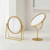 A gold-toned 360° rotating metal makeup mirror with a stand on a white surface.