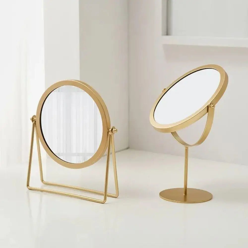 A gold-toned 360° rotating metal makeup mirror with a stand on a white surface.