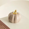 A smooth, pale beige ceramic pumpkin figurine with a gold accent sits on a white surface.