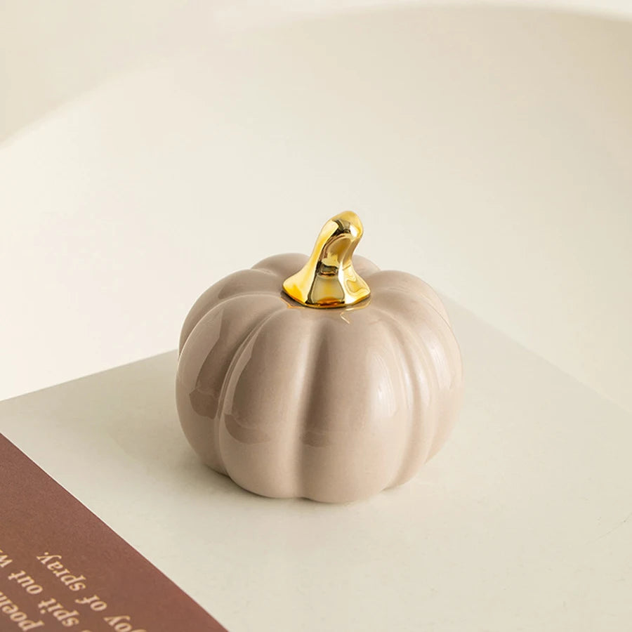 A smooth, pale beige ceramic pumpkin figurine with a gold accent sits on a white surface.