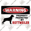 A vintage warning metal sign with red text that reads WARNING PROPERTY PROTECTED BY ROTTWEILER