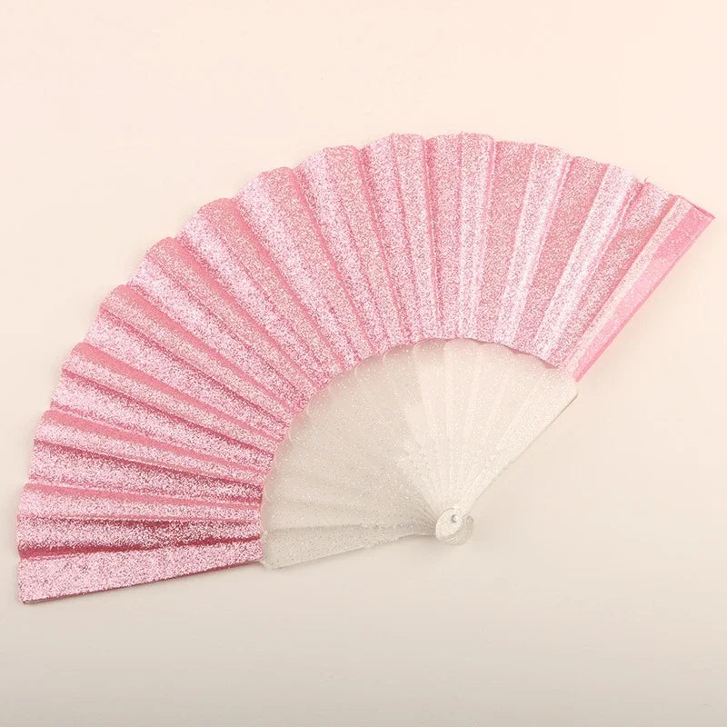 A pink glitter folding fan with transparent ribs shown in a fan shape.