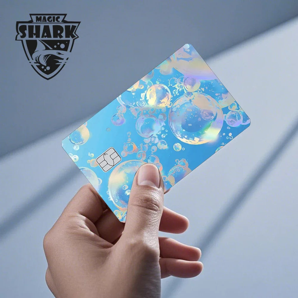 A hand holds a holographic cat credit card skin sticker displaying iridescent blue and gold colors.