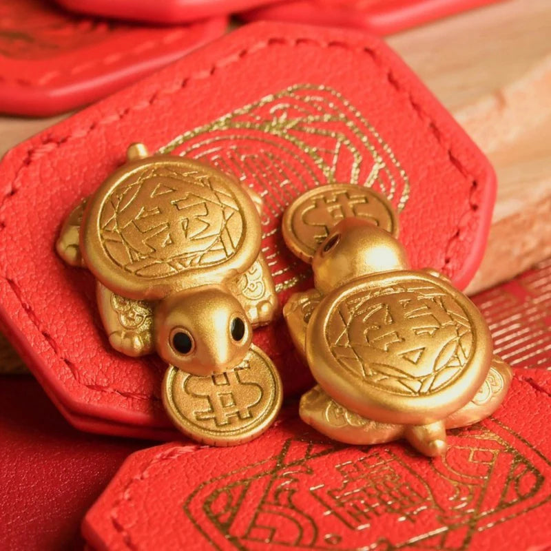 A golden tortoise figurine is displayed on a red leather card, featuring intricate patterns.