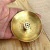 A round brass incense stick holder plate with a decorative pattern is held in a hand.