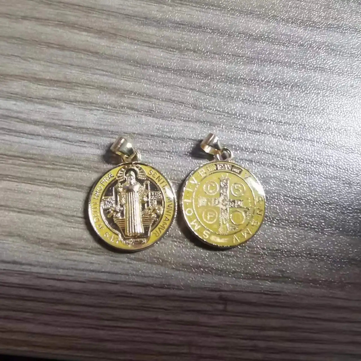 A pair of gold-colored religious pendants featuring the St. Benedict medal design.