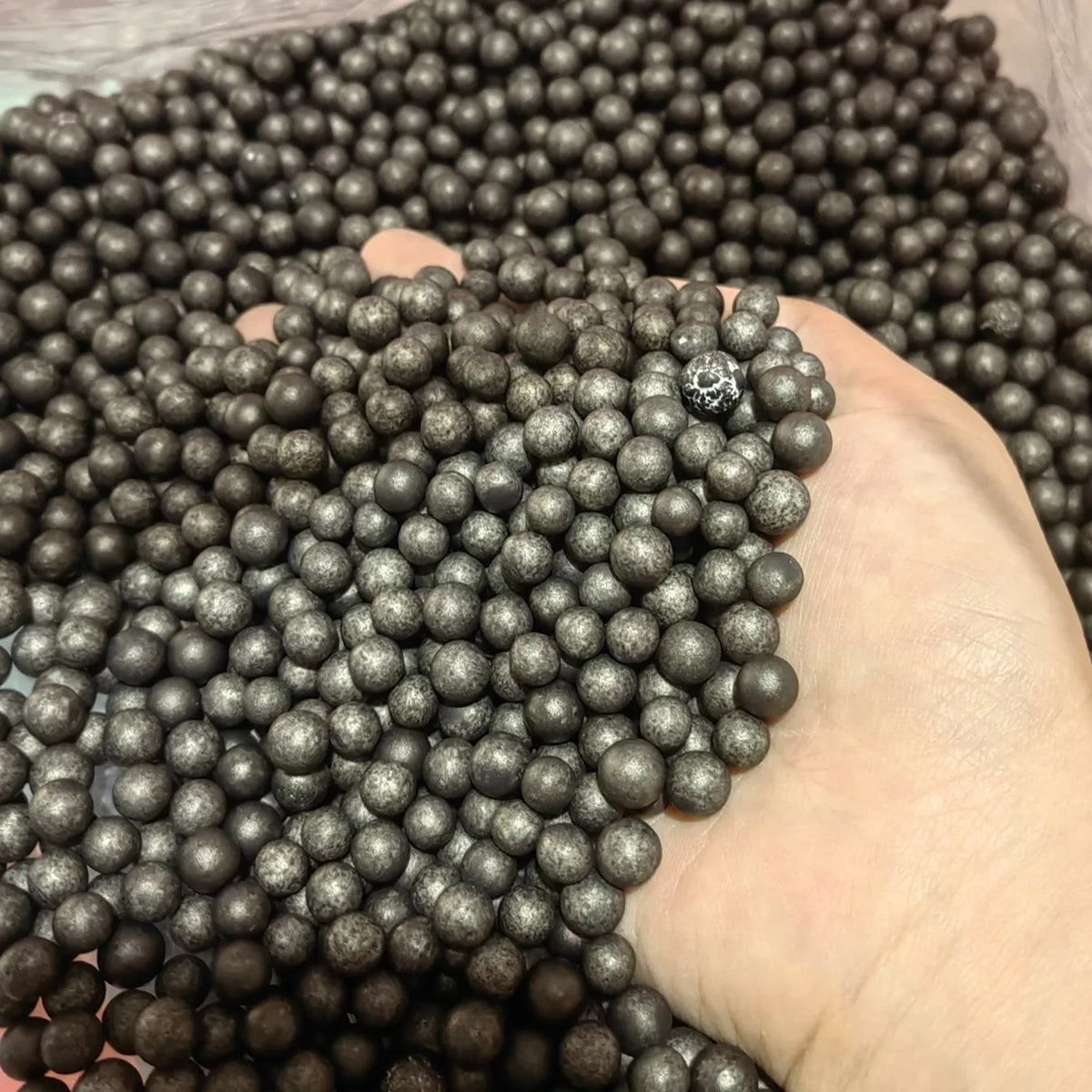 A hand is holding a large pile of dark gray foam beads for crafting and decoration.