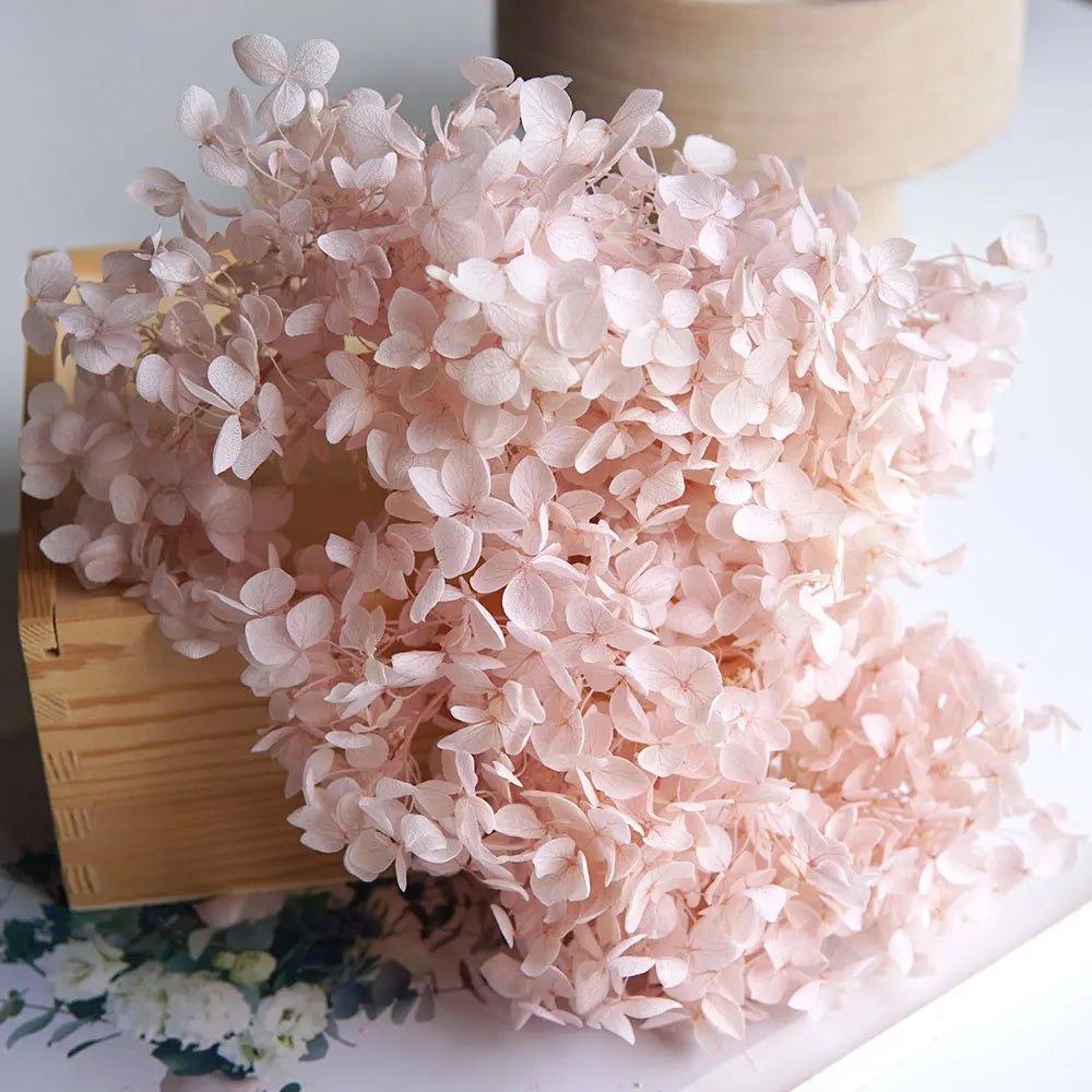 A large bunch of dried pink hydrangea florets arranged on a wooden surface.