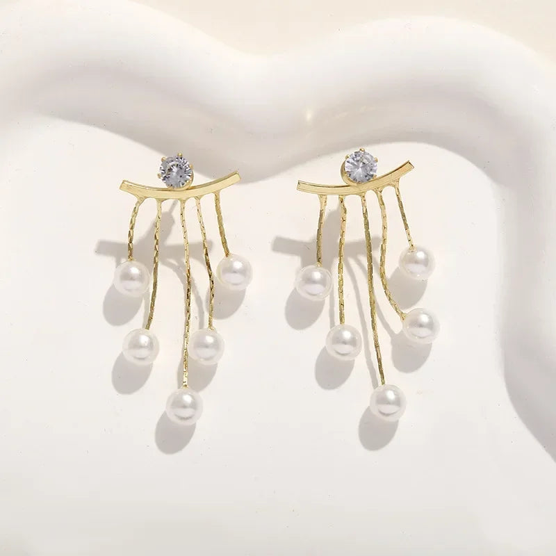 Gold-toned needle earrings featuring a diamond stud and dangling pearl tassels.