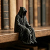 A dark, hooded figure resembling a grim reaper is sculpted as a bookend on a wooden surface.