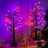 A glowing Halloween birch tree lamp with LED lights illuminates a skeleton figure in a dark setting.