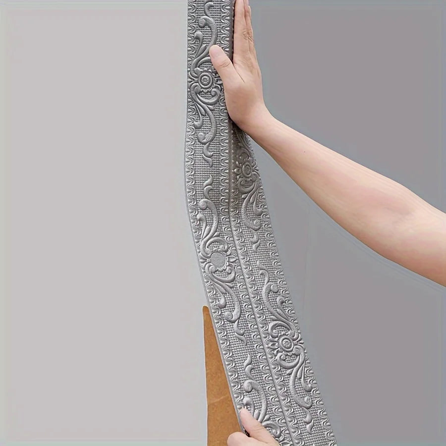 A hand is holding a long, decorative silver self-adhesive foam wall trim strip against a gray background.