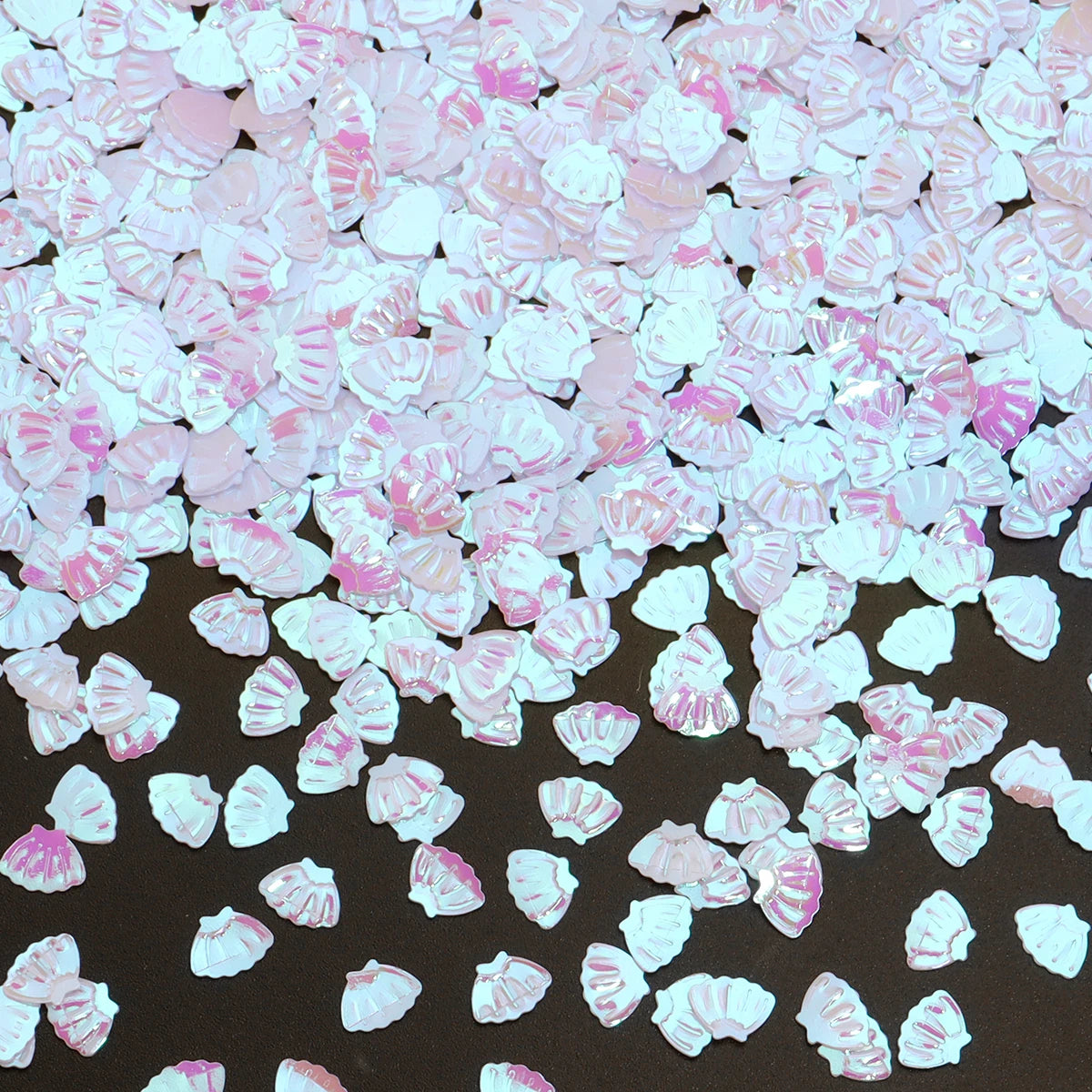 A pile of pink and white sea shell PVC sequins for nail art and craft decoration.
