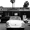 Une voiture blanche vintage est garée devant un bâtiment avec des palmiers et une enseigne.