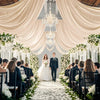 A wedding ceremony aisle decorated with white flowers and sheer fabric curtains leading to a couple.