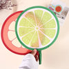 A round foldable hand fan with a green frame and a sliced citrus fruit design, held by a hand.
