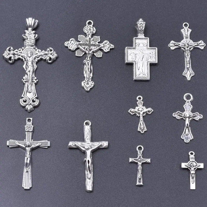 A collection of antique silver cross charms and pendants for jewelry making displayed on a dark gray background.