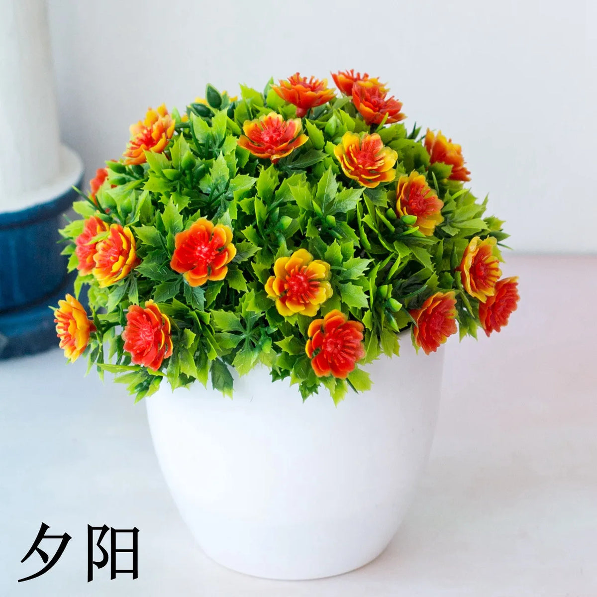 Un arrangement vibrant de fleurs de bonsaïs artificielles orange et rouge, dans un pot en céramique blanche.