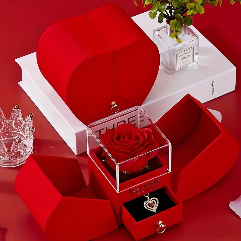 A red velvet box containing an elegant rose pendant necklace and a matching red gift box on a white surface.