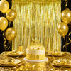 A golden sequin glitter party backdrop with hanging gold streamers and a cake on a gold-draped table.