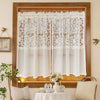 Beige sheer curtain with floral embroidery hanging in a wooden window frame.