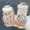 Botella reutilizable transparente llena de agua y decorada con pegatinas de estética vintage.