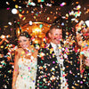 A bride and groom are showered with multicolor paper confetti during a celebration.