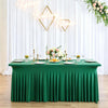 A green pleated tablecloth set for an event featuring gold geometric light fixtures and floral arrangements.