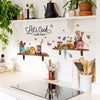 A display of cooking tools and floral wall stickers on a white shelf.