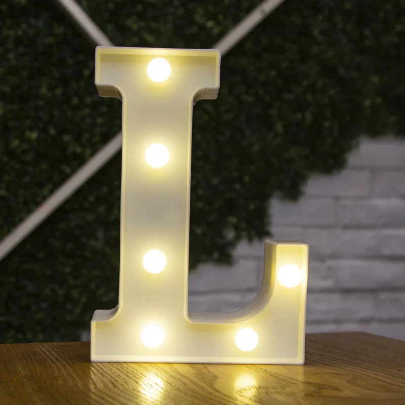 A glowing warm white LED alphabet letter light shaped like the letter L resting on a wooden surface.