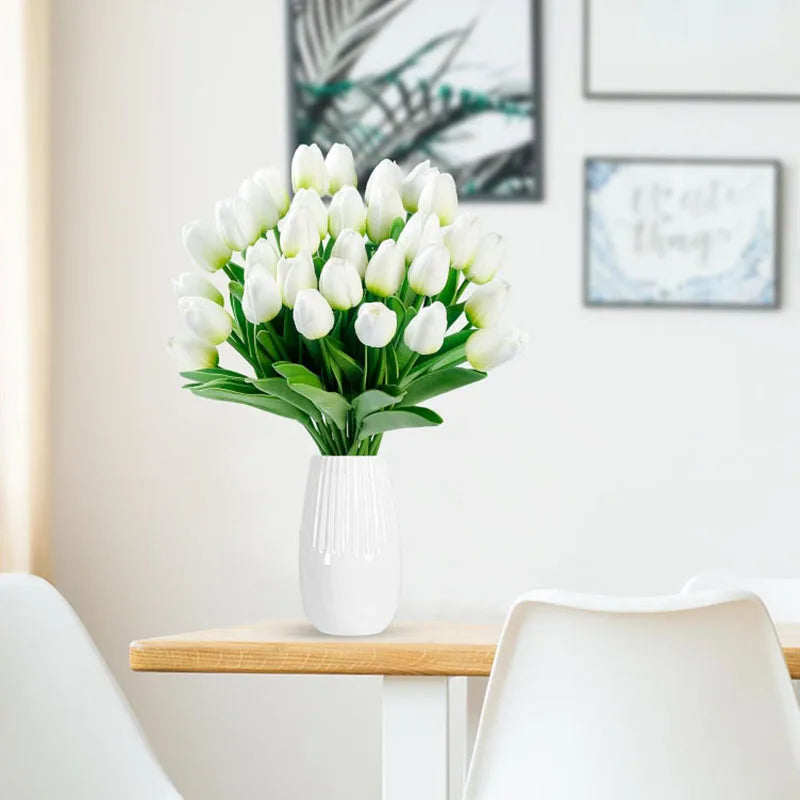 A bouquet of white tulips in a white vase displayed on a wooden table.