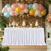 A white pleated polyester table skirt decorated with pink and yellow balloons and cake toppers for a celebration.