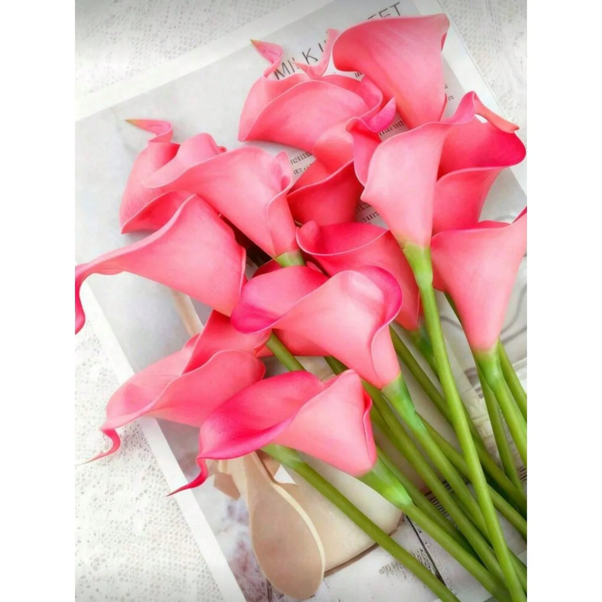 A bouquet of five vibrant pink calla lily stems with green leaves.