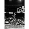 Black and white photo of a basketball player dunking during a game in an arena.