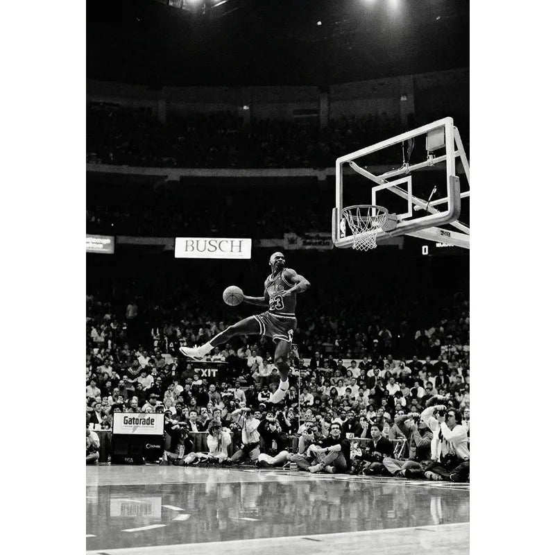 Black and white photo of a basketball player dunking during a game in an arena.
