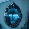A dark, ornate mirror frame featuring a face and pentagram amulet, set against a light blue wall.