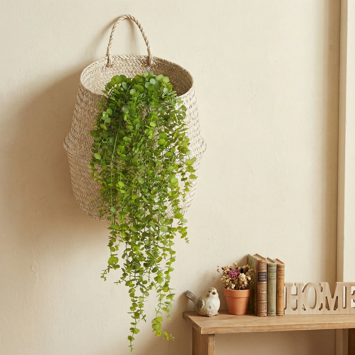 Hängende künstliche Eukalyptus-Tanne-Ranken-Dekoration in einem geflochtenen Korb an einer hellen Wand.