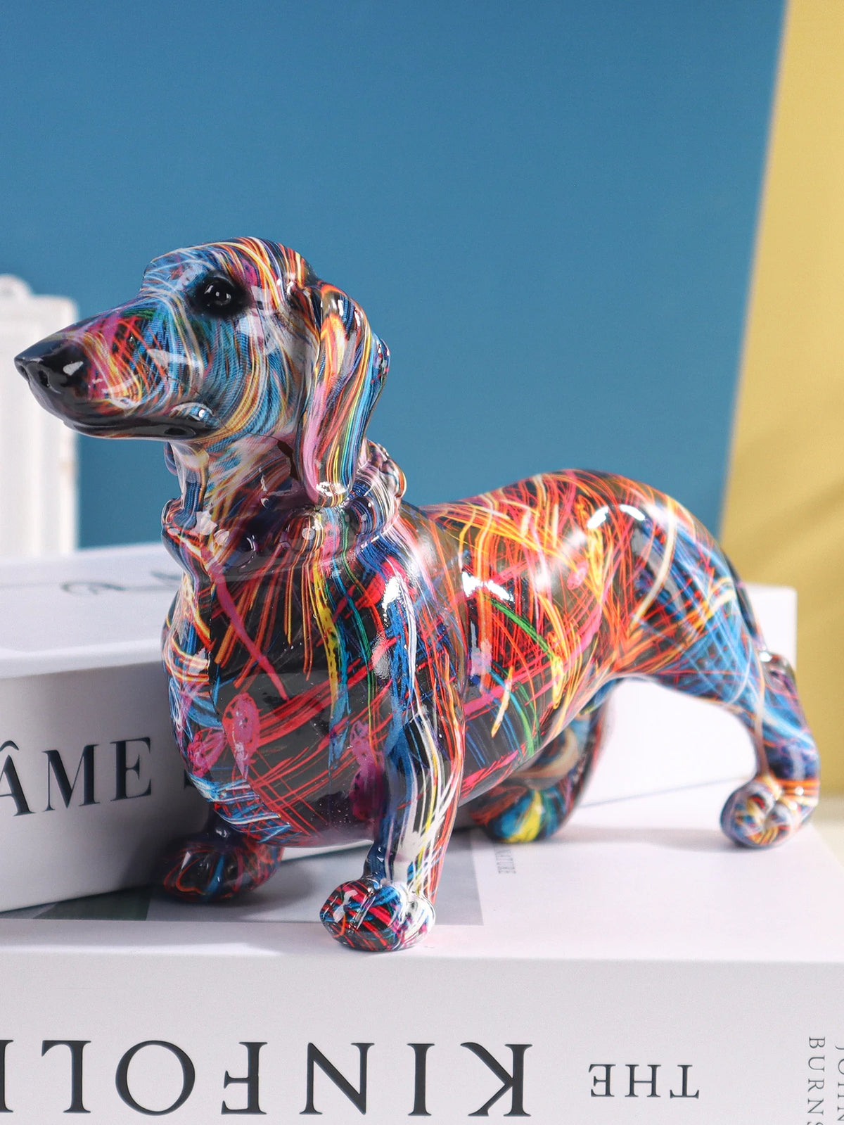A colorful resin figurine of a dachshund dog standing on a white box.