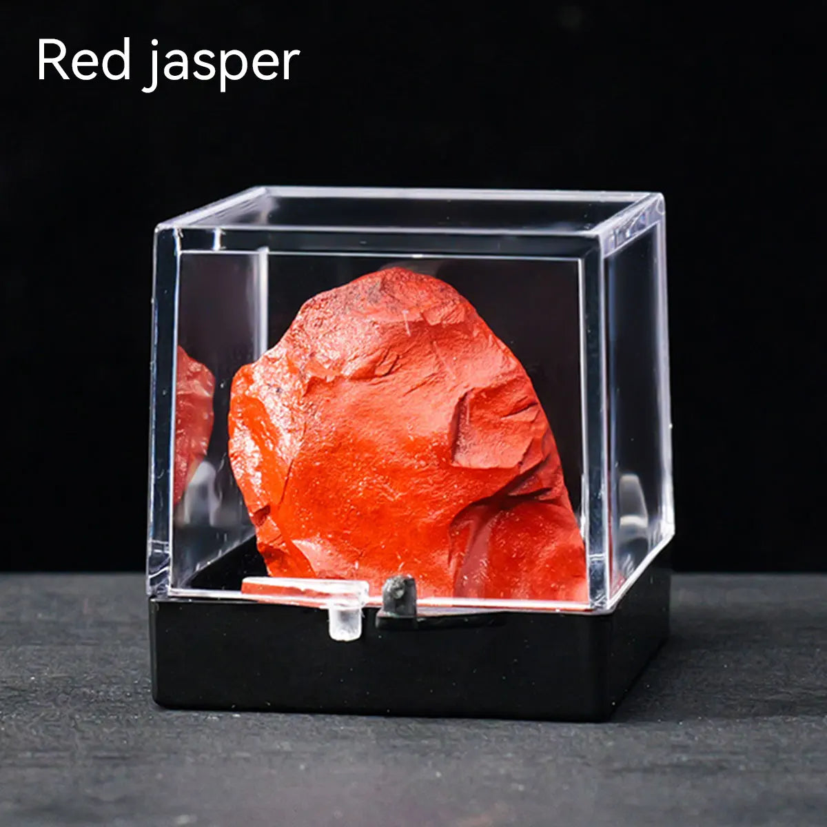 A rough, bright red jasper crystal specimen displayed inside a clear glass box.