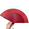 A hand holds an elegant red bamboo folding fan, showing its pleated design and classic structure.