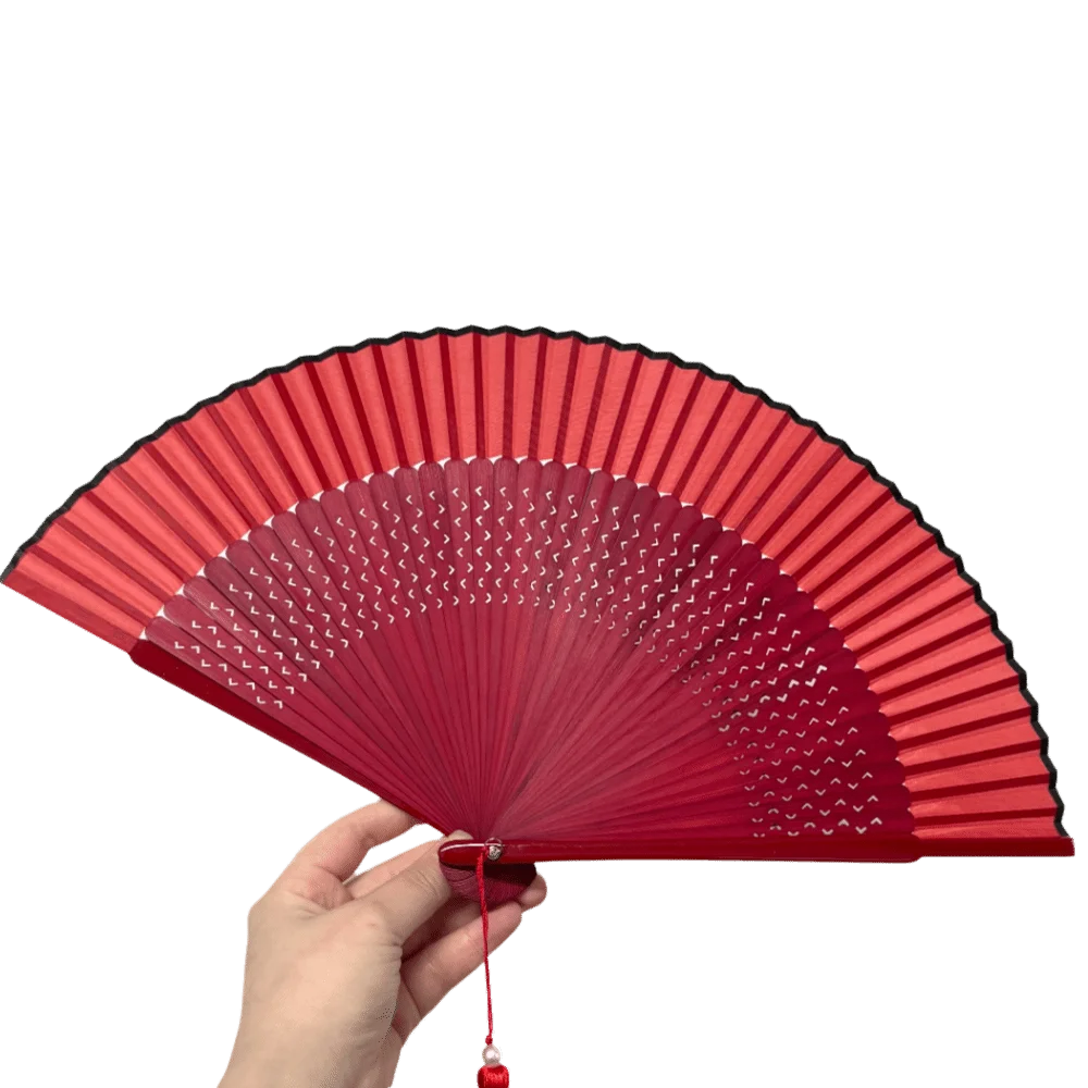 A hand holds an elegant red bamboo folding fan, showing its pleated design and classic structure.