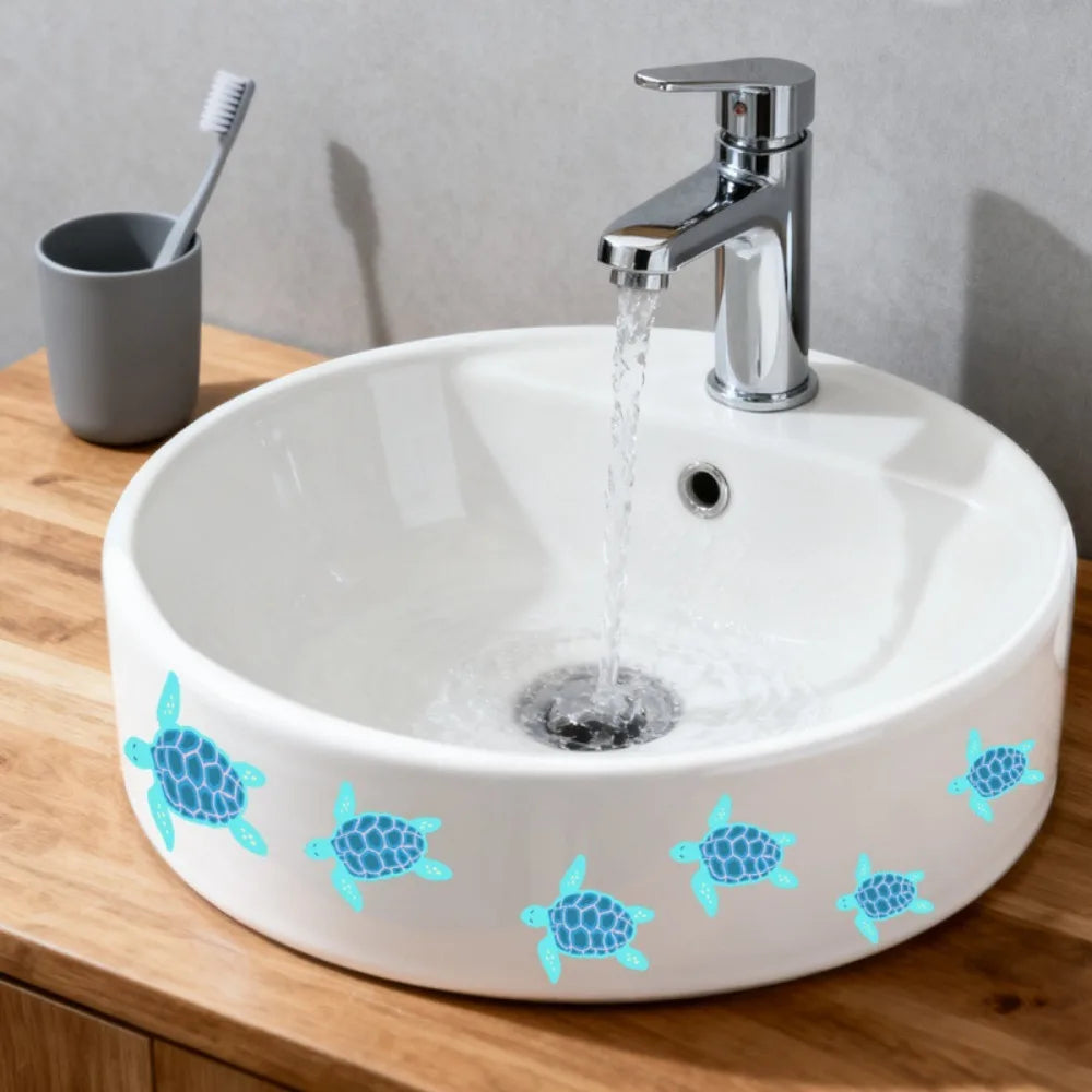 A white ceramic bathroom sink with blue sea turtle decals on the rim, next to a silver faucet and a toothbrush.