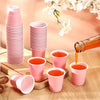 A collection of pink mini plastic shot cups and stacked pink plastic cups are displayed on a wooden surface.