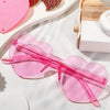 Pink rimless heart-shaped sunglasses resting on a white surface next to red hearts.