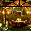 Outdoor dining scene featuring a wooden pergola with string lights illuminating a table set for dinner.