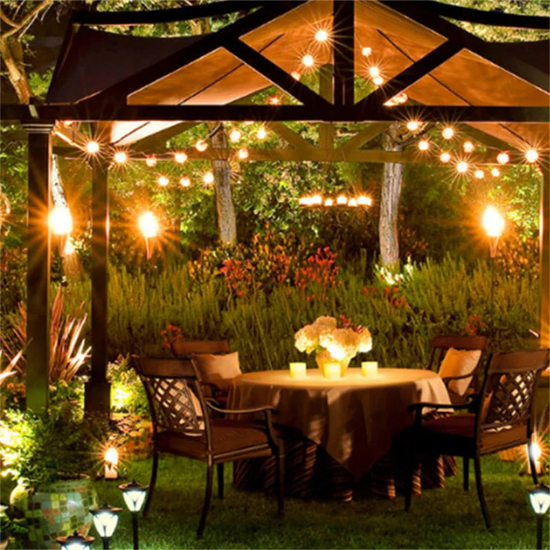 Outdoor dining scene featuring a wooden pergola with string lights illuminating a table set for dinner.
