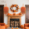 An orange pumpkin wreath decorated with autumn foliage hangs on a white wall above a fireplace.